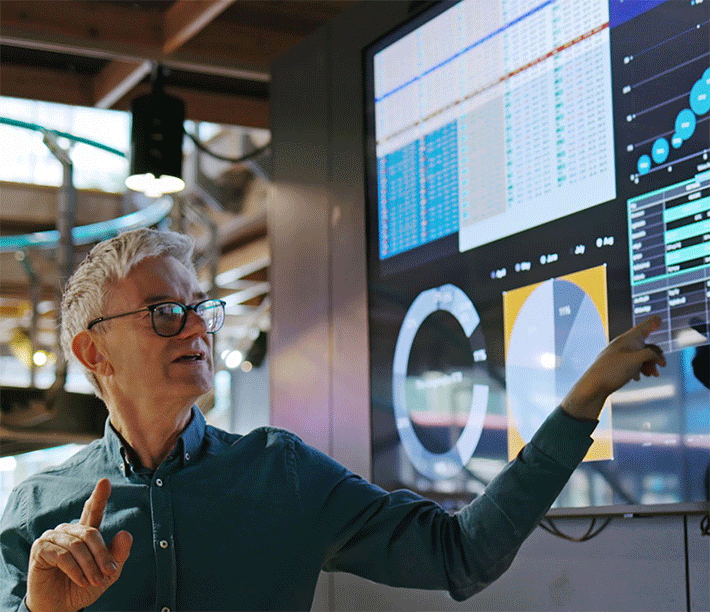 Man wearing glasses looking and pointing at a large screen