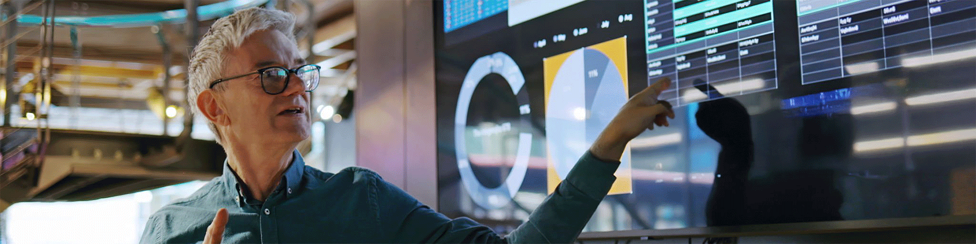 Man wearing glasses looking and pointing at a large screen