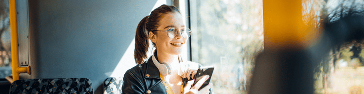 Girl on bus smiling on her phone looking out window